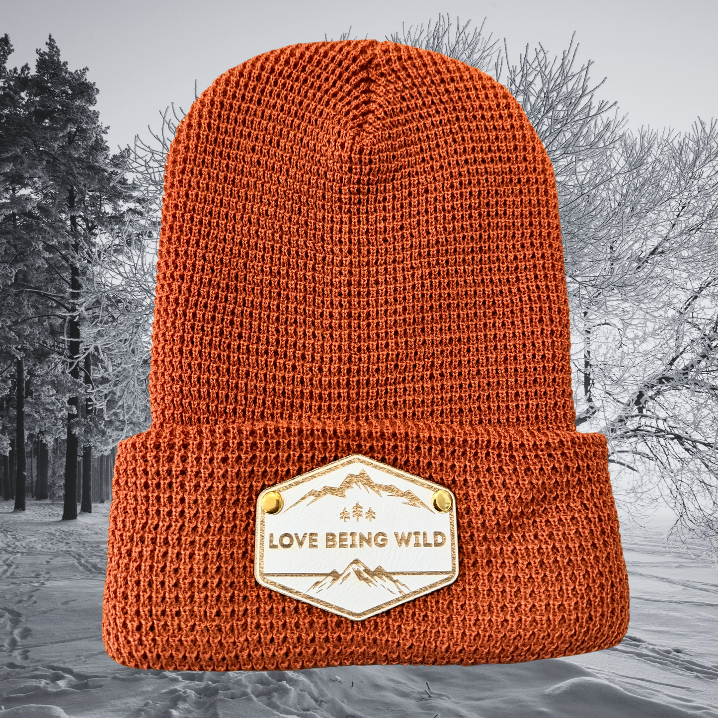 Orange knit beanie with 'Love Being Wild' patch on a snowy background