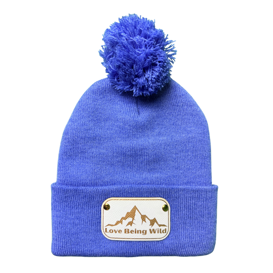Blue beanie with pom-pom and 'Love Being Wild' patch on a white background