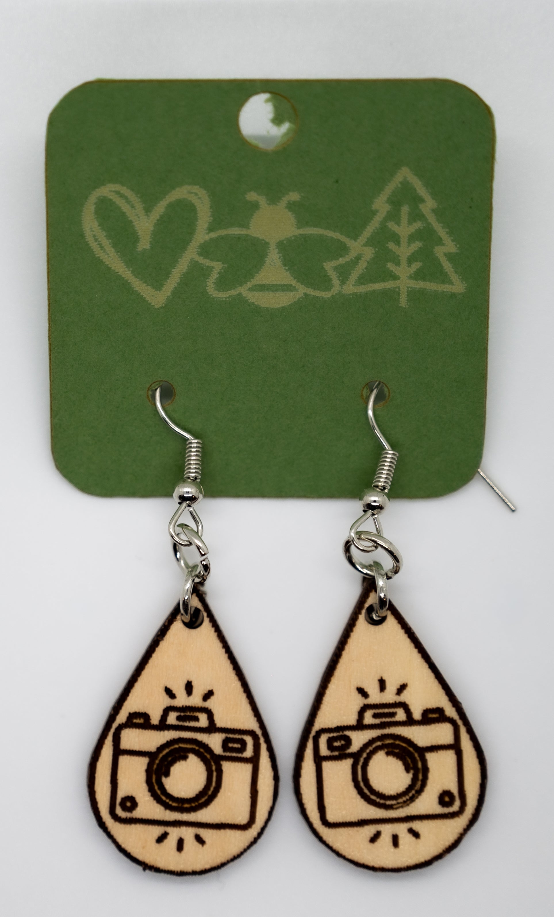 Wooden camera-shaped earrings on a green card with nature-themed designs.