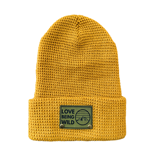 Yellow knit beanie with a patch that says 'Love Being Wild' on a white background