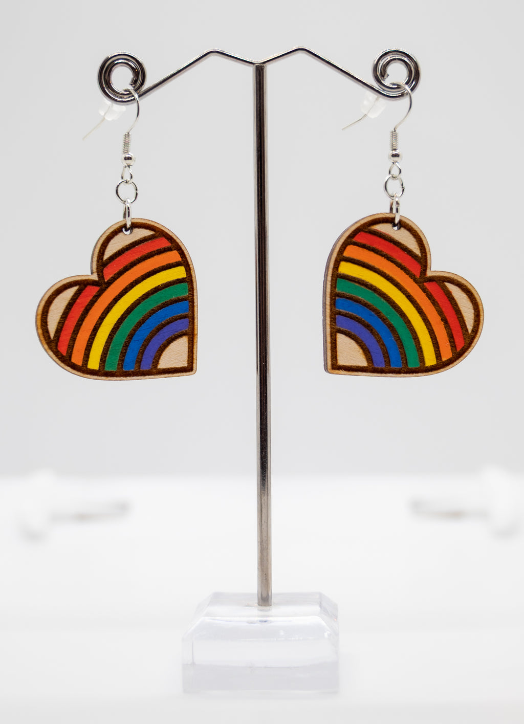 Heart-shaped rainbow earrings on a stand with a white background