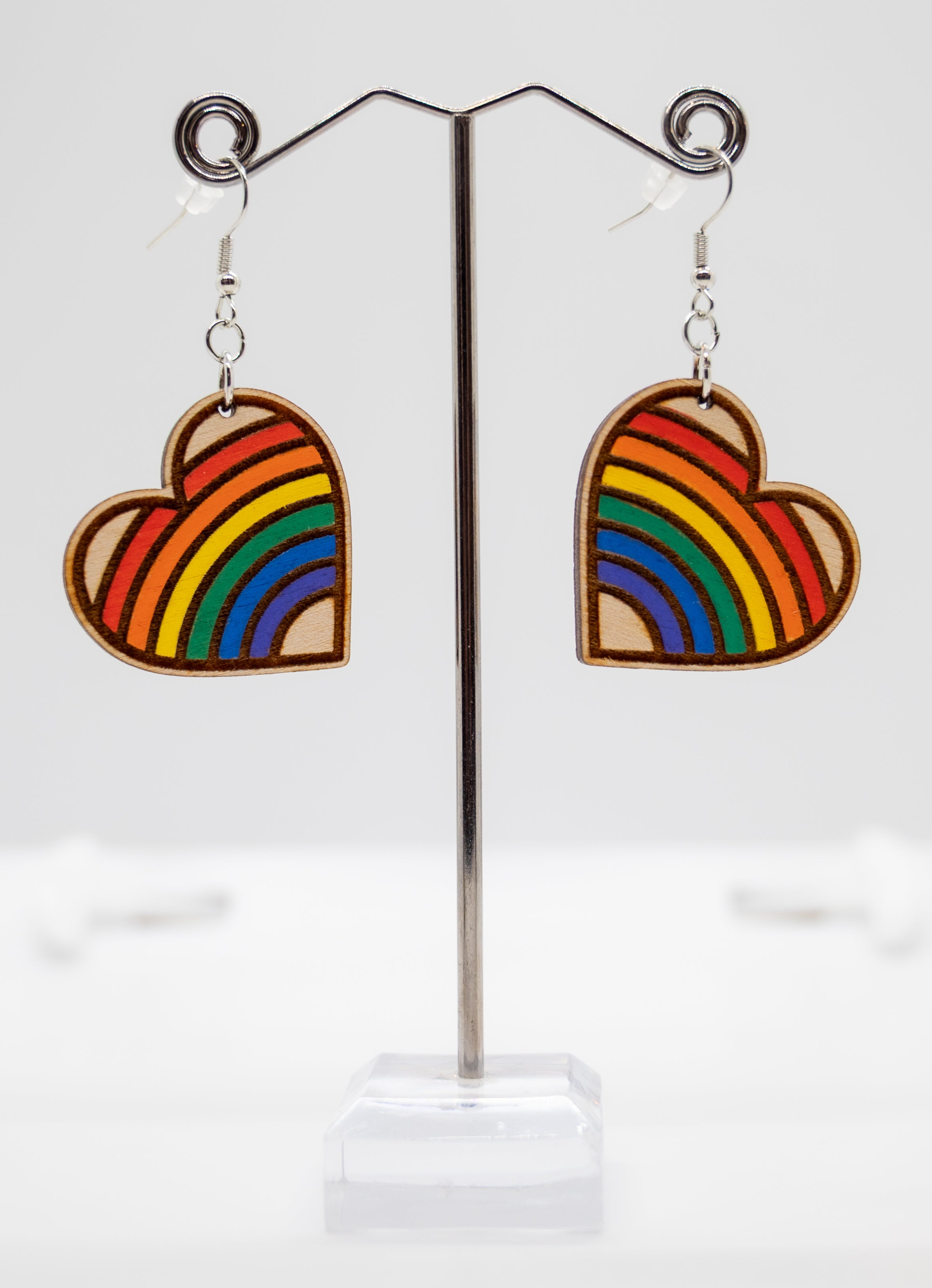 Heart-shaped rainbow earrings on a stand with a white background