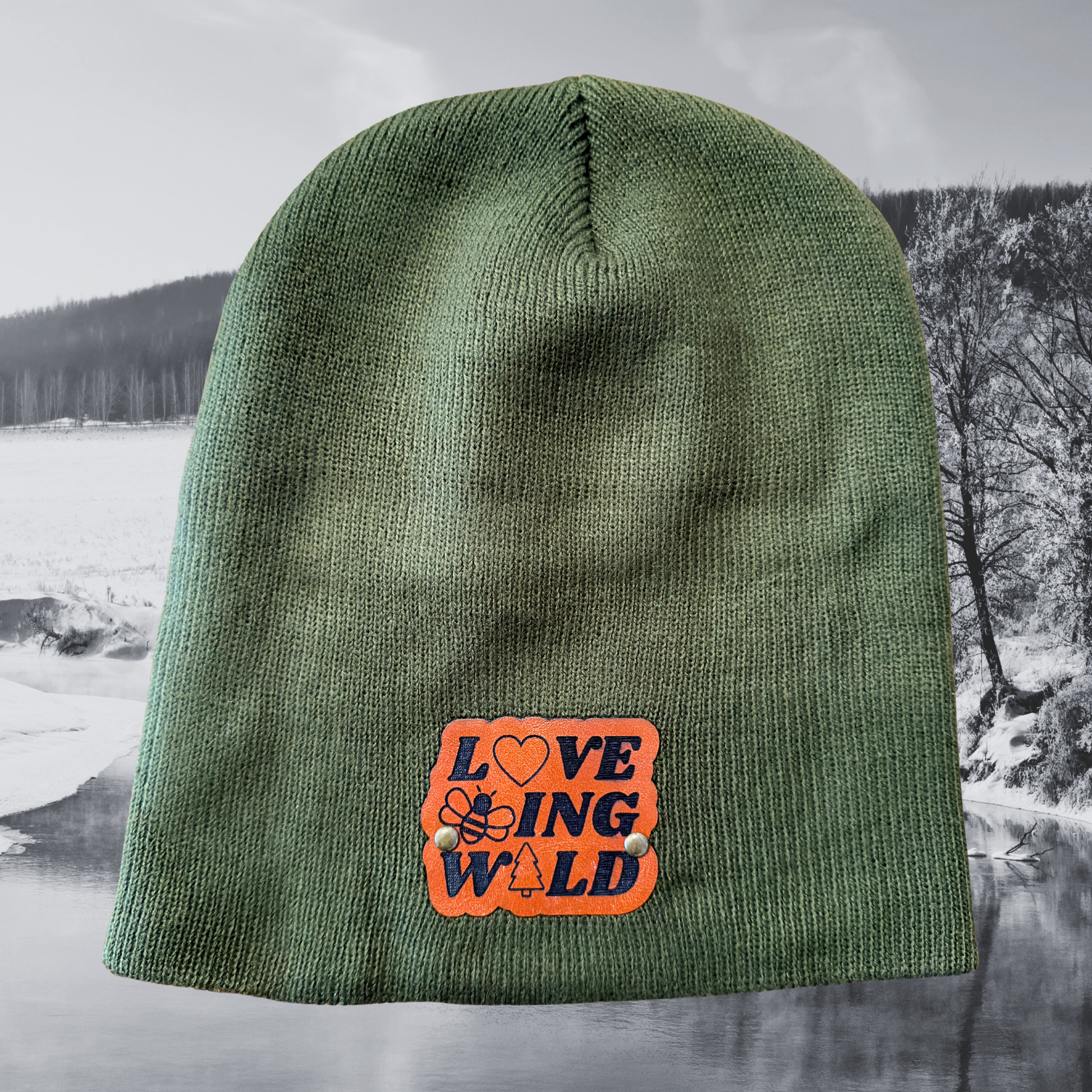 Green beanie with 'LOVING WILD' patch against a snowy landscape background