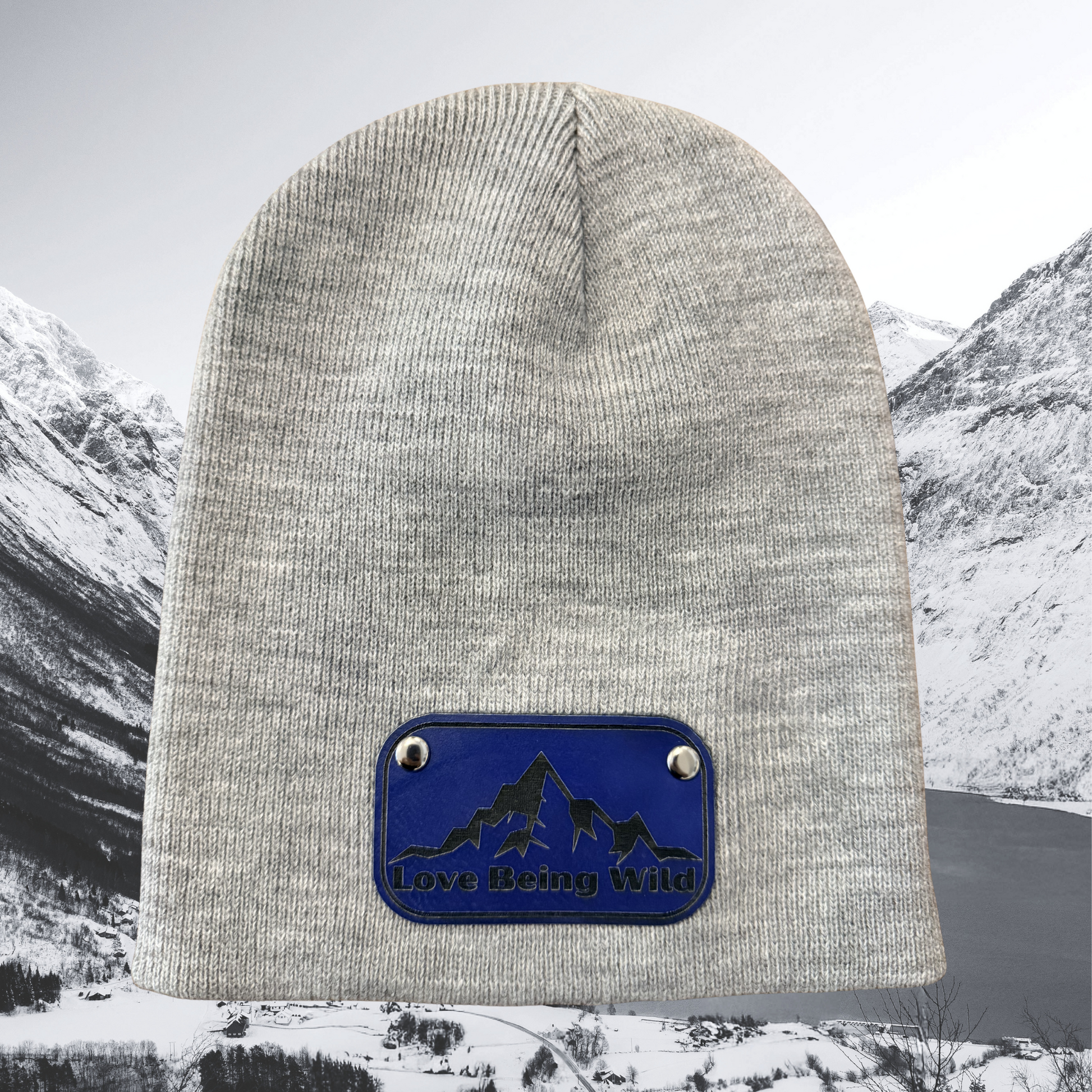 Gray beanie with a blue patch featuring mountain and dog design, set against a snowy mountain landscape.