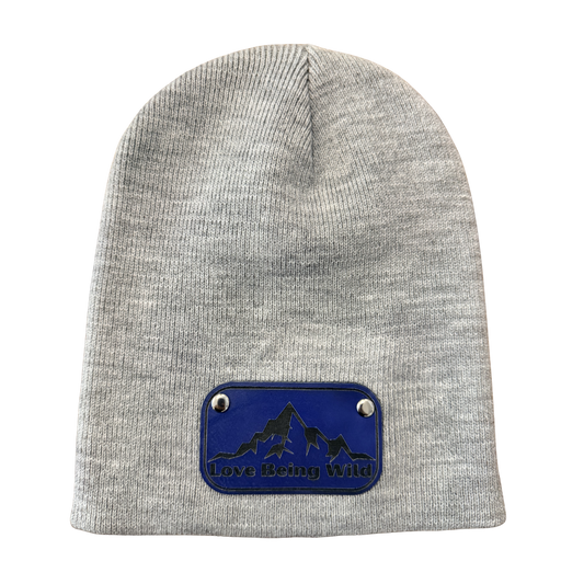 Gray beanie with a blue patch featuring mountain and dog design on a white background