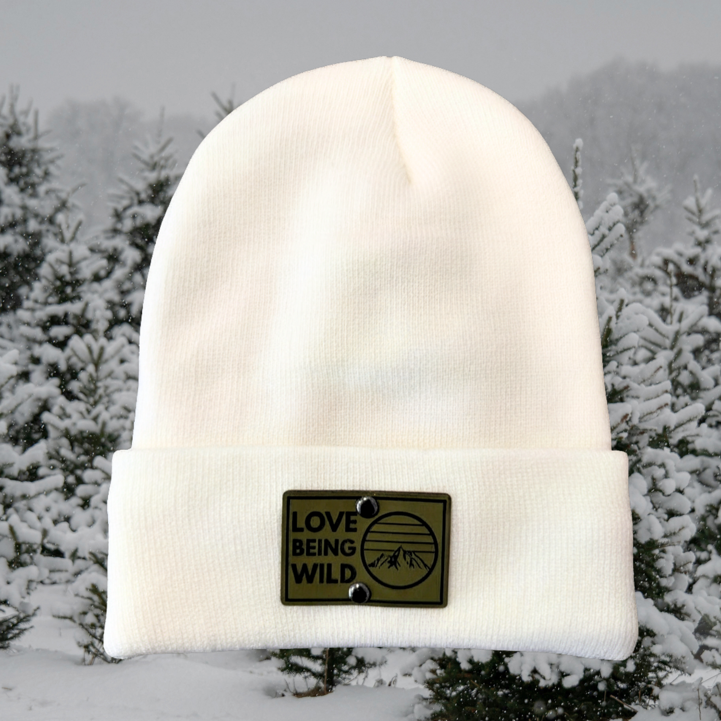 White beanie with 'Love Being Wild' patch in a snowy landscape