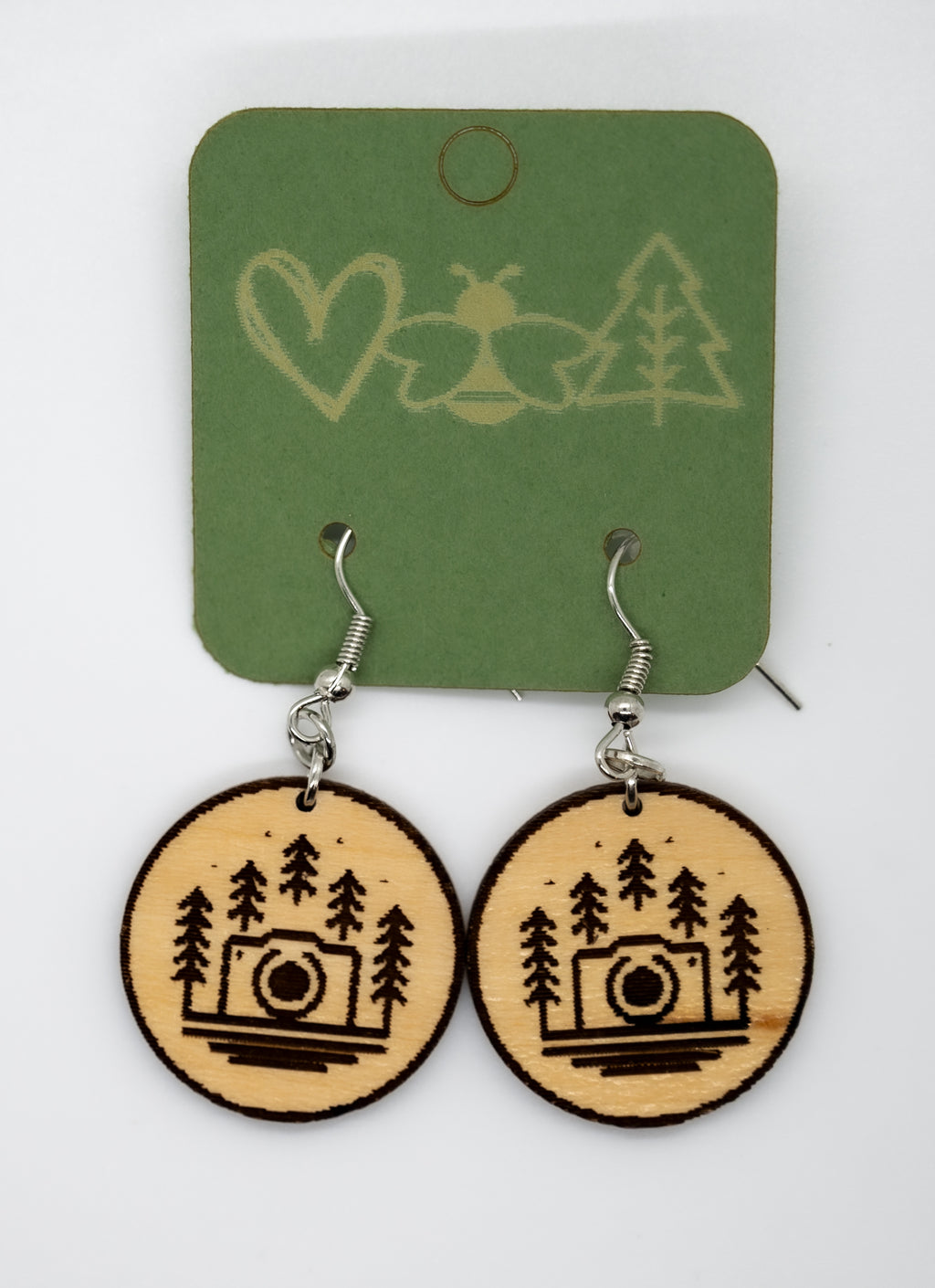 Wooden earrings with camera and tree design on a green card with nature symbols.