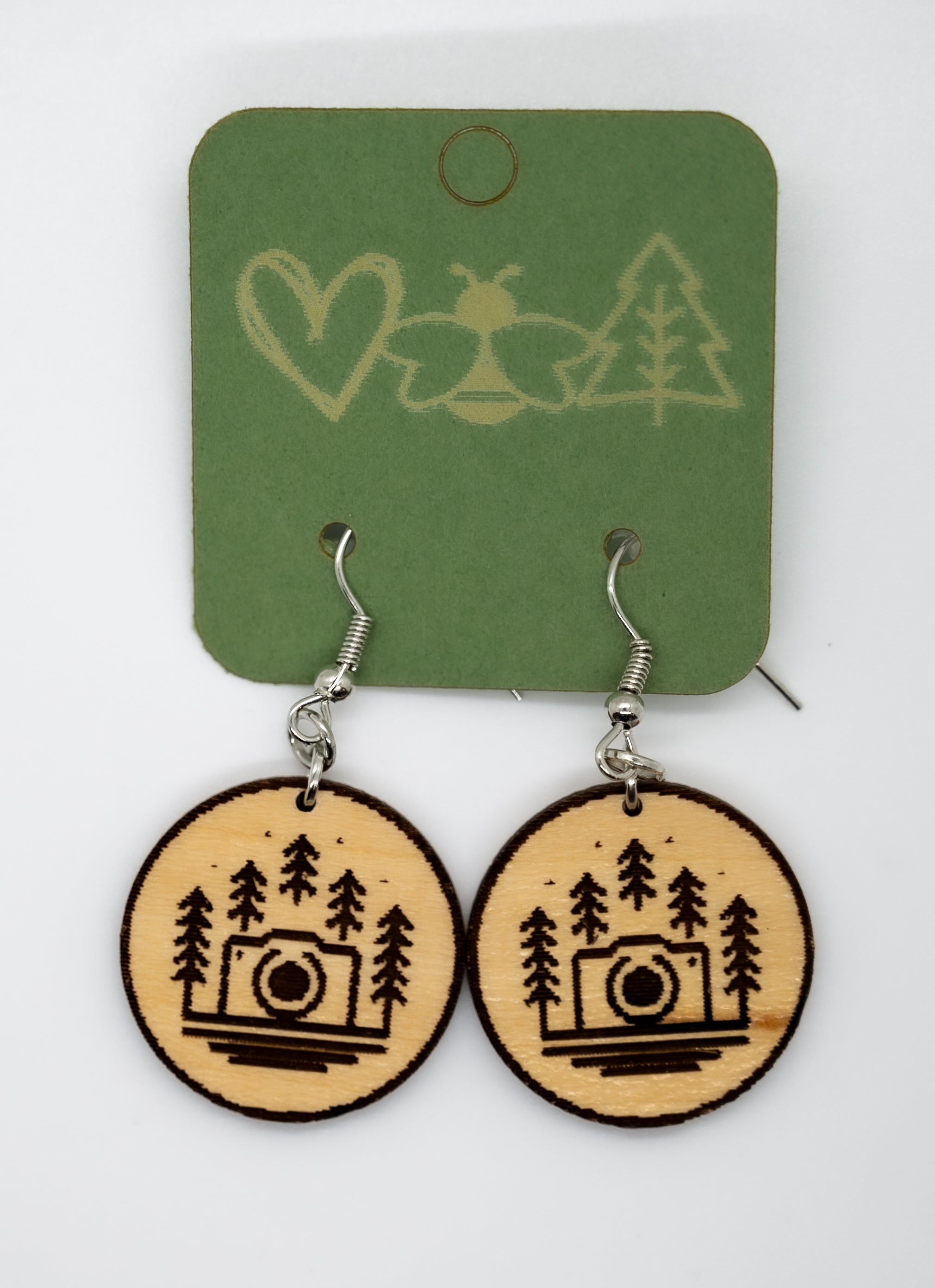 Wooden earrings with camera and tree design on a green card with nature symbols.
