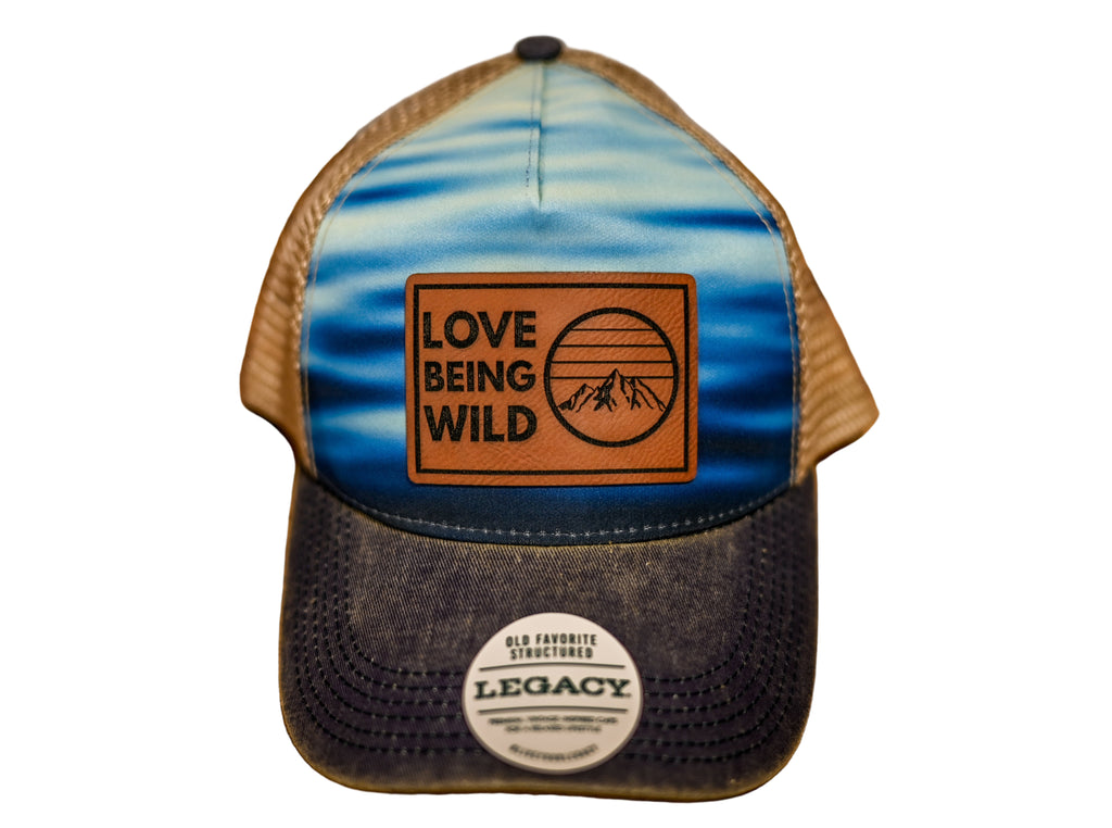 Trucker hat with 'Love Being Wild' logo and 'Legacy' label on a wooden surface