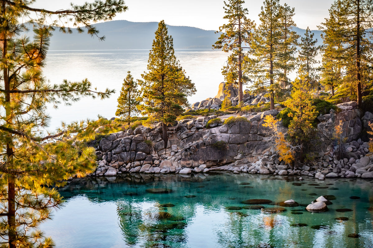 Fine art photograph of turquoise Lake Tahoe water beneath granite cliffs and sunlit pine trees.