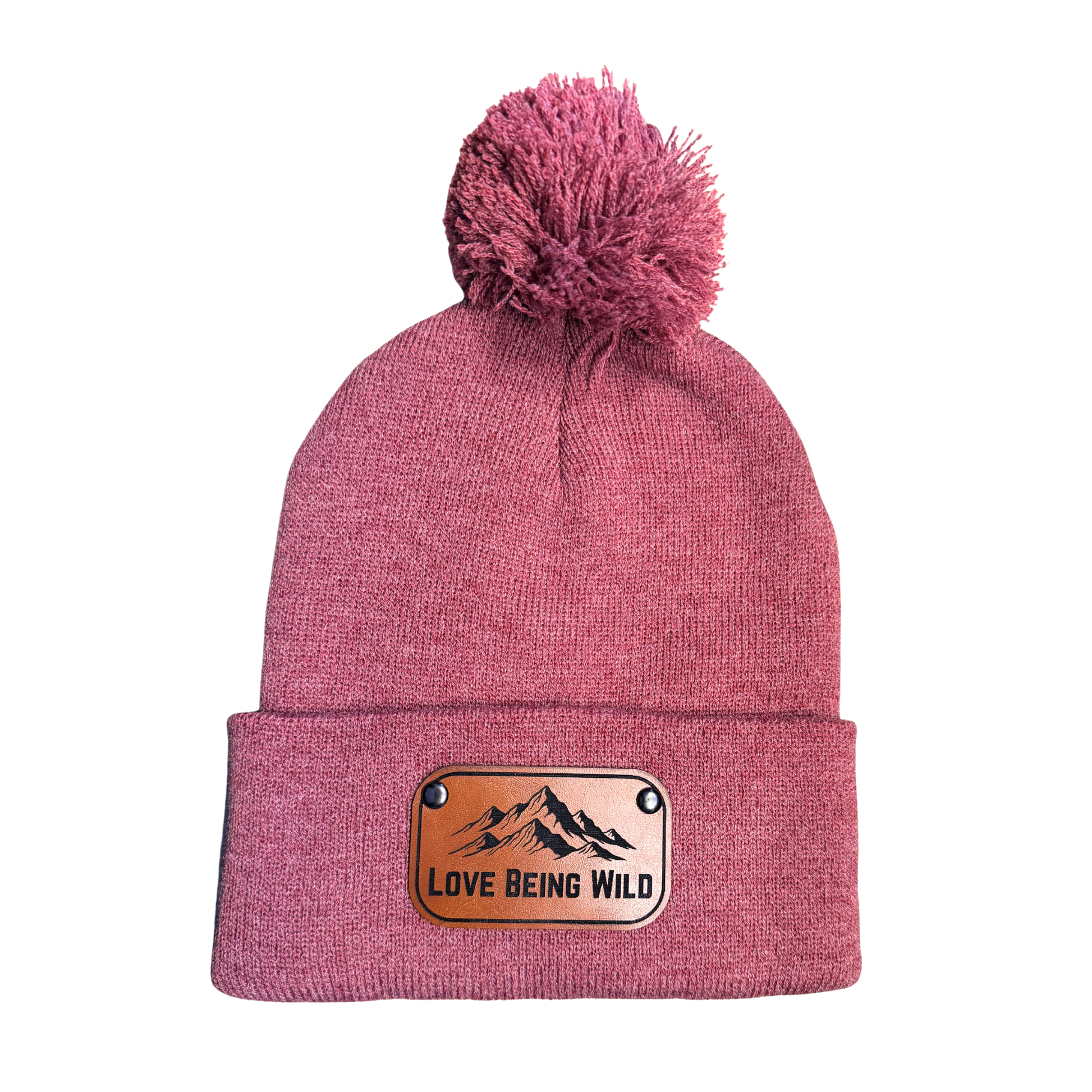 Pink beanie with a pom-pom and 'Love Being Wild' patch on a white background