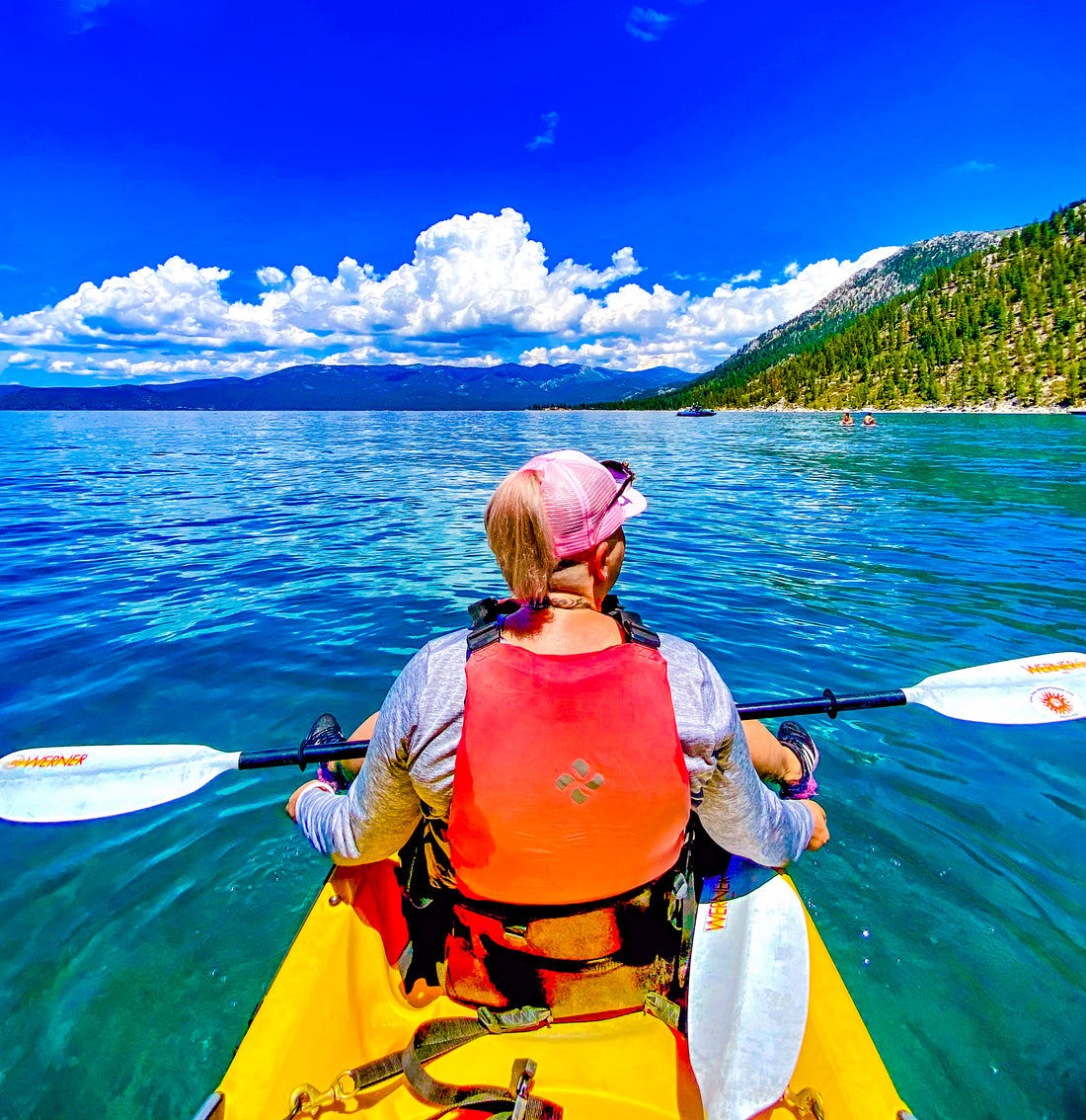Woman kayaking on Lake Tahoe with clouds and blue sky in the distance